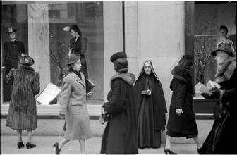 [Women walking past window displays on 5th Avenue.]