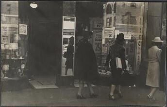 [Women walking past window display.]