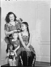 [Woman braiding a girl's hair as a younger girl holds a doll.]