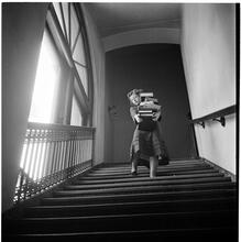 Columbia University [Woman carrying a large stack of books down stairs.]