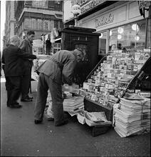 Newsstand [People browsing through magazine racks at a busy sidewalk newsstand.]