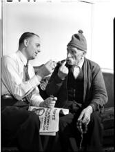 [Man lighting another man's pipe.]