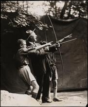 [Two Boy Scouts helping Al Smith fire a bow and arrow.]