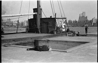 [Destitute man sleeping on East River pier with Brooklyn skyline visible.]