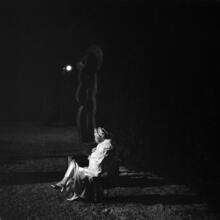 [Woman sitting in MoMA sculpture garden at night.]