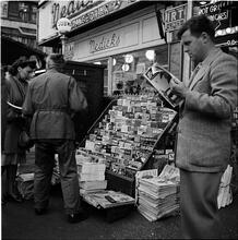 Newsstand [People browsing through magazine racks at a busy sidewalk newsstand.]