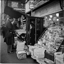 Newsstand [People browsing through magazine racks at a busy sidewalk newsstand.]