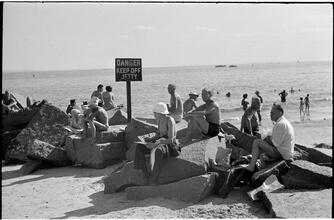 [Sunbathers ignoring warning sign and relaxing on jetty.]