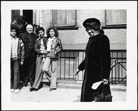 Priest and teens on sidewalk with African- American woman walking by
