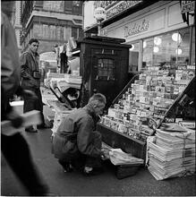 Newsstand [People browsing through magazine racks at a busy sidewalk newsstand.]