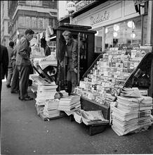Newsstand [People browsing through magazine racks at a busy sidewalk newsstand.]