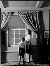 [Girl and boy looking out a window.]