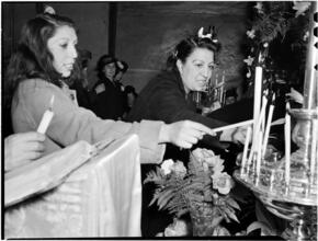[Women lighting candles from an altar.]