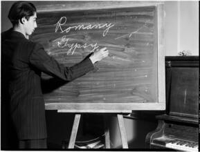 [Young man writing "Romany Gypsy" on a blackboard.]