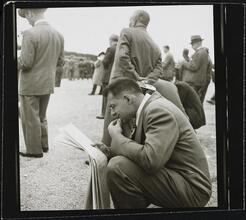 Aqueduct Race Track [Man crouched, reading a newspaper.]
