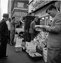Newsstand [People browsing through magazine racks at a busy sidewalk newsstand.]