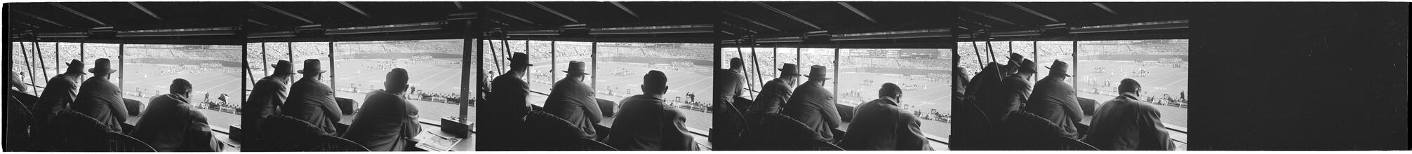Football Writers [Reporters commentating on a football game in a stadium from the press box.]