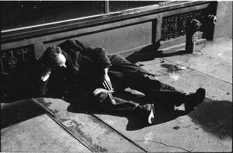 [Destitute man sleeping on sidewalk.]