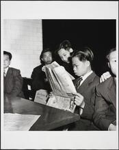 [Young Chinese man reading a newspaper at Ellis Island.]