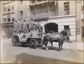 [Firemen riding in a horse-drawn fire cart.]