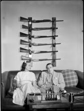 Billy Rose [Billy Rose and Eleanor Holm on a couch in front of a gun rack.]