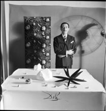 Salvador Dali: Rugs [Salvador Dali standing in front of a rug he designed near a table with objects.]