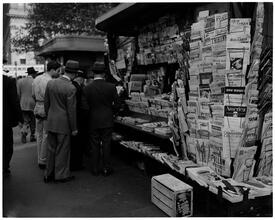 Newsstand [People browsing through magazine racks at a busy sidewalk newsstand.]