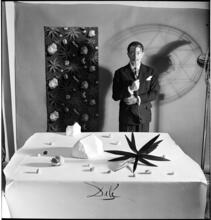 Salvador Dali: Rugs [Salvador Dali standing in front of a rug he designed near a table with objects.]