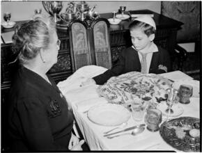 [Boy and an older woman at a ceremonial dinner.]