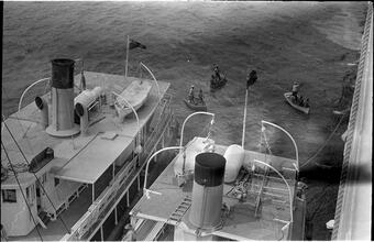 [Aerial view of men rowing boats next to larger vessels.]