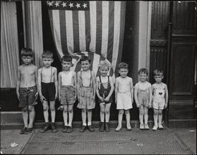 View of children of graded heights in front of the American flag, Victory celebrations
