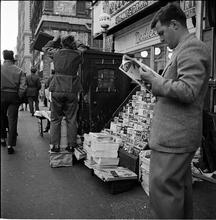 Newsstand [People browsing through magazine racks at a busy sidewalk newsstand.]