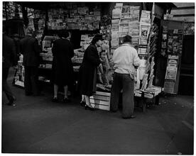 Newsstand [People browsing through magazine racks at a busy sidewalk newsstand.]