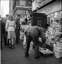 Newsstand [People browsing through magazine racks at a busy sidewalk newsstand.]