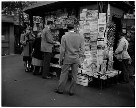 Newsstand [People browsing through magazine racks at a busy sidewalk newsstand.]